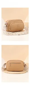 Detail of light brown crossbody bag featuring dual zippers and woven patterned strap