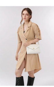 White envelope shoulder bag with gold chain strap shown on a model in trench dress