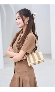Detail of straw woven crossbody bag featuring vertical beige and brown stripes