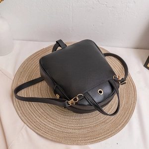 Mini black synthetic leather backpack for women with gold metal hardware on straw mat