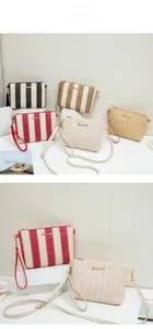Detail of woven straw envelope bags with metal zipper and adjustable straps in various stripes