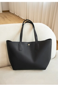 Détail d'un sac cabas trapèze en cuir noir avec bouton doré sur un canapé crème
