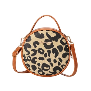 Round leopard print crossbody bag with brown faux leather handles and detachable strap