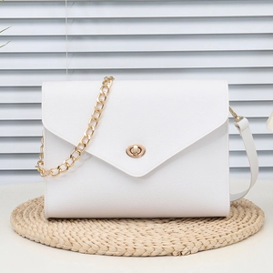 White pebbled leather envelope crossbody bag with gold chain and twist lock on a woven mat