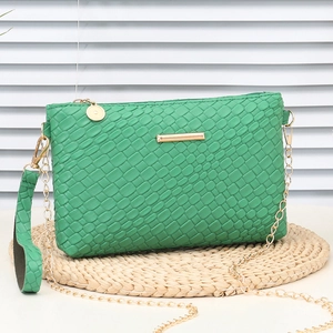 Mini green woven handbag with golden chain strap and textured handle on woven mat