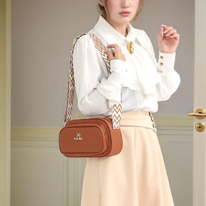 Women's brown pebble leather crossbody bag with wide geometric strap and gold logo