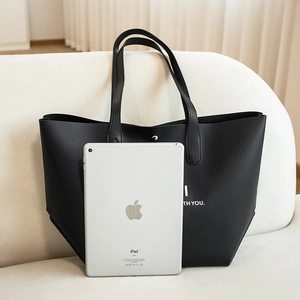 Grand sac cabas en cuir noir avec lettrage blanc et bouton-pression doré sur canapé