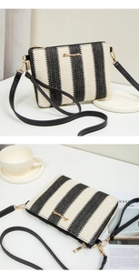 Detail of woven black and white striped crossbody bag with golden logo and zipper closure