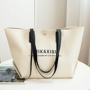 Minimalist beige tote bag with black handles and artistic letter print in soft lighting