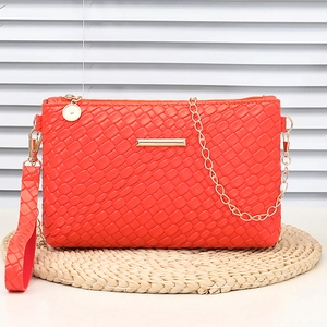 Orange woven leather crossbody bag with gold chain and wrist strap on a straw mat