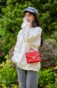 Detail of red crocodile texture handbag with gold chain strap held by a model outdoors
