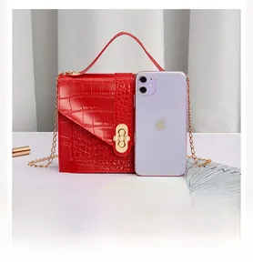 Size comparison of a red croc-embossed small square bag next to a smartphone