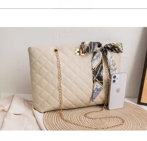 Close-up of beige quilted handbag with gold chain, twist lock, and decorative silk scarf