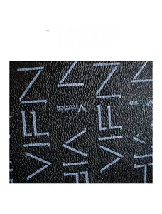 Macro shot of black pebbled leather texture with white geometric lettering on crossbody bag