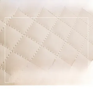 Macro shot of beige quilted faux leather fabric with premium white stitching details