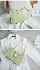 Detail view of a light green crocodile texture handbag with white resin and gold chains