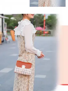 Detail of plaid tote bag with orange leather flap and circular metal buckle on chic floral outfit