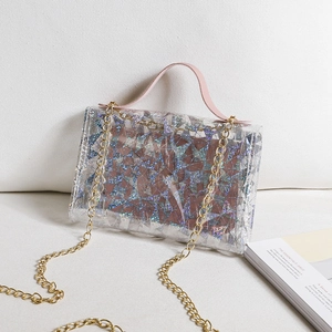 Mini sac transparent à paillettes laser avec poignées roses et chaîne dorée sur canapé