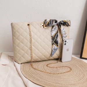 Quilted beige tote bag with gold chain straps and geometric scarf detail on woven mat