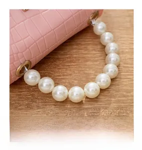 Detail of pink faux crocodile leather bag with large pearl handle and gold metal rings