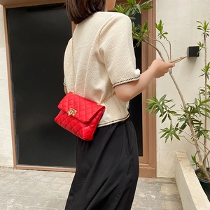 Chic red quilted shoulder bag with gold chain strap shown on a model outdoors