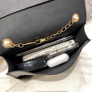 Minimalist black mini bag with gold chain showing internal storage for phone and makeup