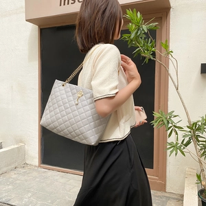 Large grey quilted tote bag with gold chain strap and crown pendant shown on a model