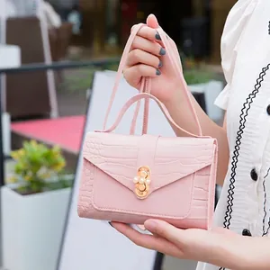 Pink faux crocodile leather mini handbag with pearl buckle and shoulder strap held by hand