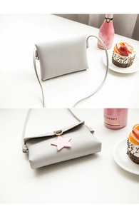 Detail of grey synthetic leather mini bag with pink star charm on a bright white table