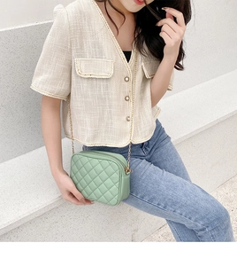 Close-up of mint green quilted camera bag with gold chain strap on a minimalist bench
