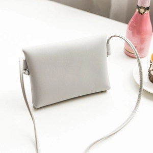 Minimalist light grey crossbody bag in pebble grain leather on a cozy white desk
