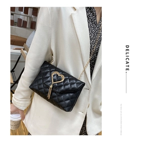 Detail of black quilted chain bag with gold heart clasp and tassel on a beige blazer
