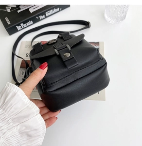 Close-up of black litchi pattern crossbody bag with metal buckle on a minimalist desk