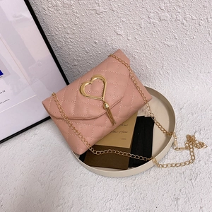 Sac bandoulière rose matelassé avec boucle cœur dorée et pompon dans un décor élégant