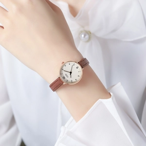 Vintage women's watch with brown leather strap and rose gold round case on white shirt