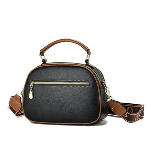Detail of black pebbled leather handbag with brown trim and patterned fabric strap
