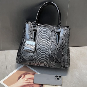Detail of silver python print handbag with glossy black handles and mini charm bag