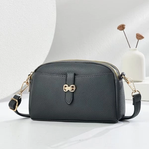 Detail of lychee textured leather crossbody bag with golden bow clasp and double zippers