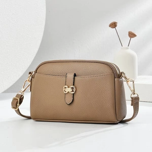 Brown lychee grain leather crossbody bag with golden hardware in a minimalist white setting