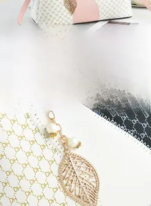 Detail of white leather bag with DH pattern and golden leaf pendant with pearls