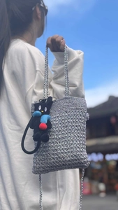 Detail of silver crochet tote bag with a black cat plush charm against the sky