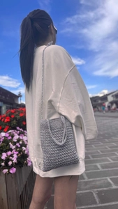 Detail of silver crochet crossbody bag showing tight knit texture against a blue sky