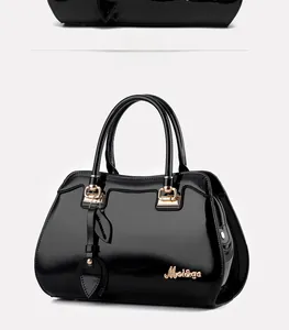 Detail of glossy black patent leather handbag featuring gold metal clasp and logo