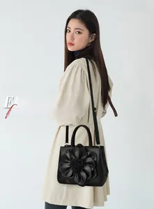 Detail of black crossbody bag featuring large 3D leather flower on Asian model in trench coat
