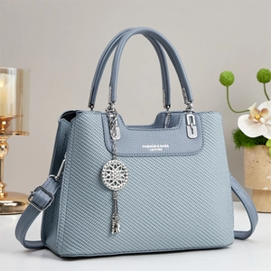 Detailed view of gray-blue woven leather handbag with fashion logo and flower pendant