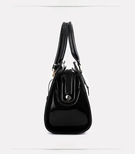 Detailed view of black patent leather handbag with glossy finish and gold metal hardware