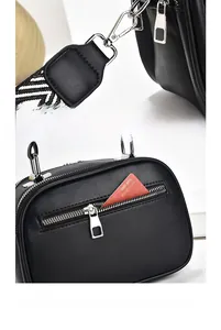 Detail of silver clasp on black leather bag with striped strap and rear zip pocket