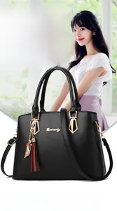 Detail of black leather handbag featuring gold cat charm and red tassel accessory