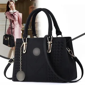 Macro detail of black leather tote featuring V-shaped stitching and gold-tone metal charms