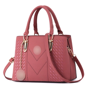 Detail of rose red leather tote bag showing V-shaped stitching and golden hardware charm